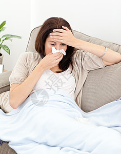 疲倦的女人在吹鼻涕时感觉到自己的体温药片休息药品组织厌倦疾病客厅沙发流感说谎图片