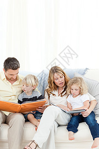 家人在沙发上读书孩子男孩们女性拥抱微笑父母家庭女孩们阅读图书图片