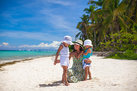 妈妈和孩子年轻母亲和两个女儿在阳光明日的奇异海滩上异国假期海岸线海岸成人晴天热带情调女士孩子背景