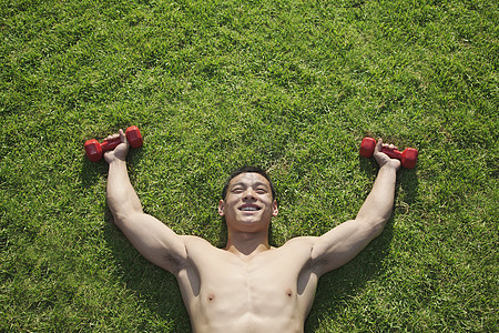 在北京和哑铃一起在草地里躺着的不穿衣服的人运动员肌肉膀子享受能力年轻人力量微笑红色运动图片