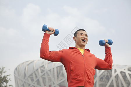 年轻男子在北京公园与哑铃一起运动微笑重量外观能力服装红色享受力量黑发福利图片