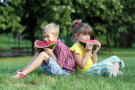 男孩和女孩坐在草地上吃西瓜图片