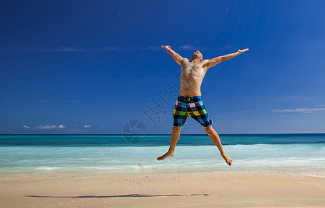 男人在海滩上跳跃蓝色游泳衣闲暇力量自由旅行身体太阳喜悦成功图片