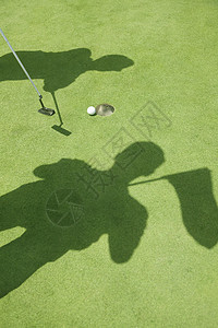 两个高尔夫球手在高尔夫球场打球的影子 洞里的球图片