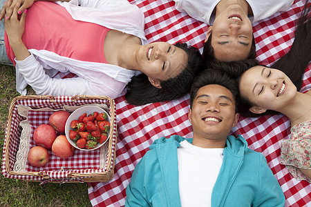 四位笑着的年轻朋友 带着头顶触摸和躺在背上在公园野餐图片