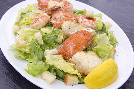 凯撒沙拉 与大虾鲑鱼和白鱼午餐蔬菜黑色盘子白色敷料食物起动机面包块餐厅图片