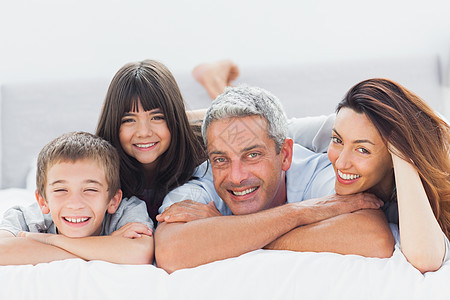 可爱的家庭躺在床上 对着镜头微笑图片