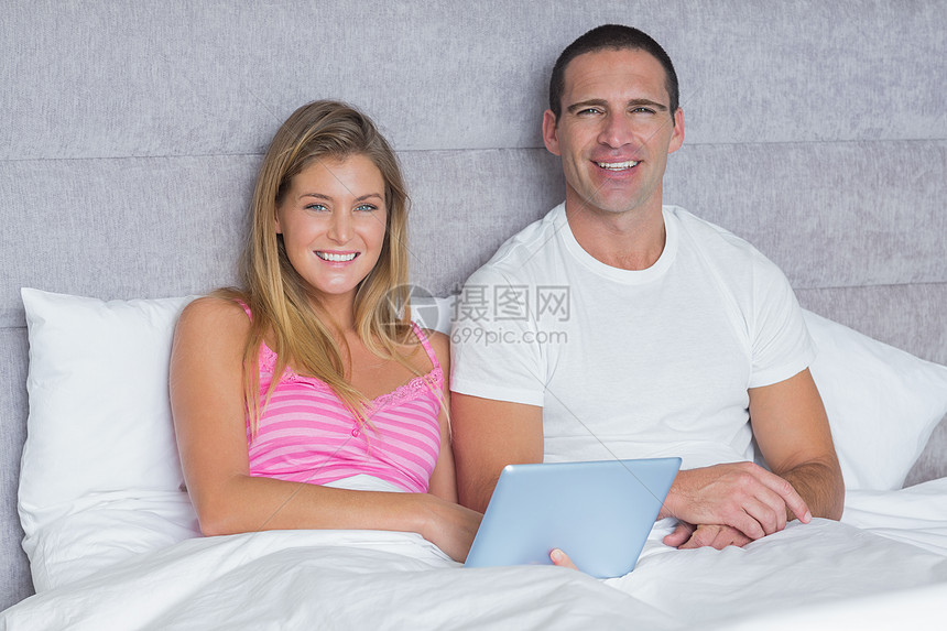 快乐的年轻夫妇在床上一起使用平板电脑图片