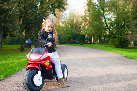 穿着皮夹克的小漂亮摇滚女孩 坐在玩具摩托车上坐着图片