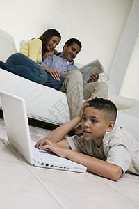 在客厅用笔记本电脑的男孩 父母在沙发地面观光图片