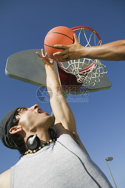 年轻人与朋友在蓝天上打篮球的低角度视角视图图片