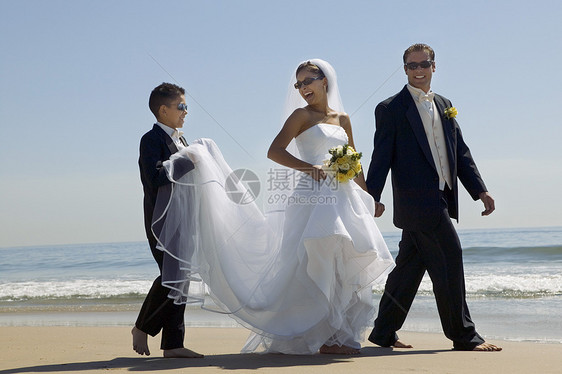 与兄弟在海滩上散步的新娘和Groom图片