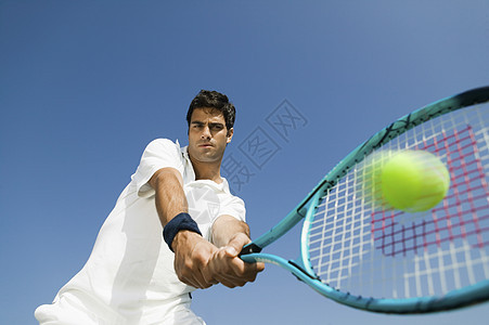 在蓝天上打网球的坚定青年男子的低角度视角图片
