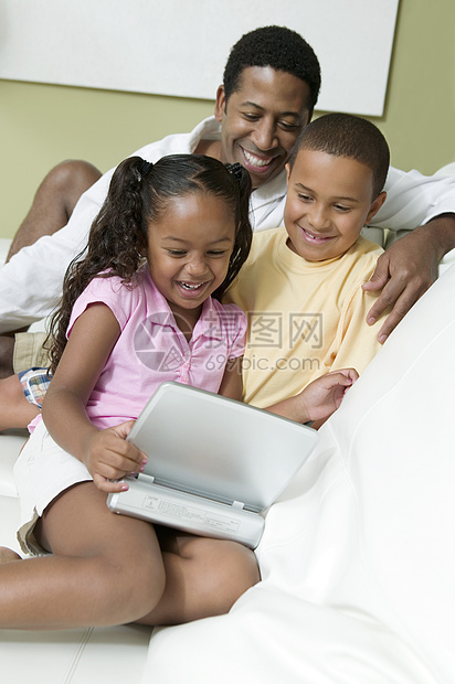 父亲与儿子和女儿在客厅看便携式DVD播放机的电影图片