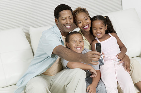 使用相机电话在沙发上用手机的家庭照片图片