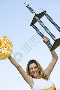 一位激动人心的啦啦队长在天上举着奖杯的肖像图片