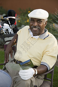 老人高尔夫快乐的高级男高尔夫球手肖像 记分卡坐在椅子上背景