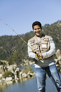 快乐的西班牙裔成熟男子在阳光明媚的日子钓鱼的肖像图片
