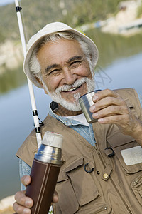 一个快乐的老人在钓鱼时 从热水瓶里喝咖啡的肖像图片