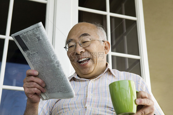 年长者在家门前喝着咖啡杯的阅读报纸图片