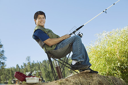 一个快乐的人坐在可折叠椅上钓鱼的肖像图片