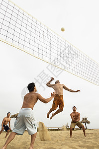 年轻男性朋友在海滩玩排球的低角度视角图片
