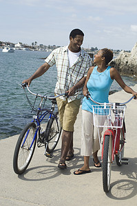 一对非裔美国人夫妇骑着自行车在海滩上看对方 并用自行车走路图片