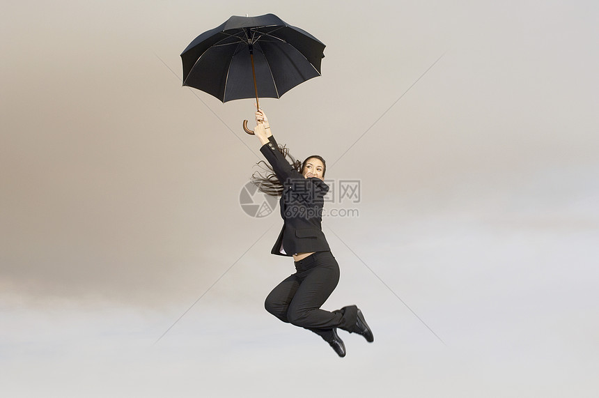 一位快乐的女商务人士在半空中拿着雨伞的全景图片