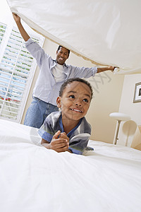 快乐的父亲拿着床单 在他小儿子的床上图片