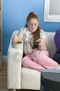 肥胖少女坐在沙发上 在吃宝石时握着遥控器图片