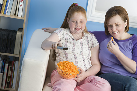 超重女孩和母亲在沙发上看电视图片