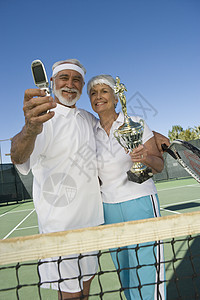 拥有奖杯和照片的网球运动员成人闲暇胜利老人退休夫妻幸福网球场手机服装图片