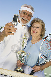快乐的老年情侣和奖杯 在网球场通过手机自画像图片