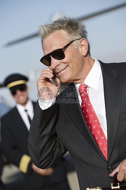 快乐的高级商务人士使用手机与飞机机长在机场的背景背景中进行电话交谈图片