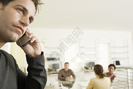 利用移动电话与同事在背景中讨论的深思熟虑的生意人图片