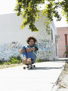 坐在城市街头滑板上坐着的全年青年男子图片