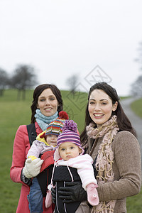 两名年轻母亲的肖像及其婴儿在公园中的婴儿图片