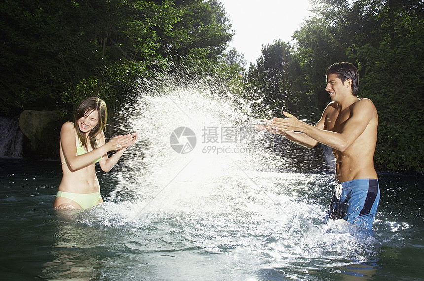 快乐的年轻男人在河里向少女泼水喜悦运动男朋友夫妻眼睛青少年女朋友乐趣喷涂男性图片