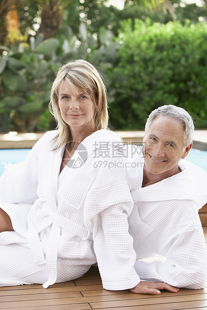 穿着浴袍坐在游泳池旁的快乐中年夫妇的肖像图片