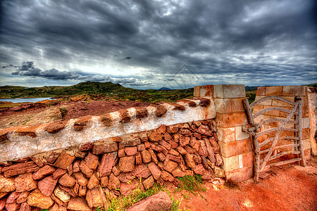 在Menorca带栅栏门的红披萨红色石墙草地植物岛屿草原岩石石头国家草本植物场地天空图片