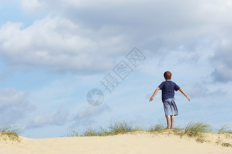看着一个小男孩站在沙丘上 用伸展的手臂挡风图片