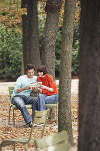 年轻夫妇阅读关于沿树干边公园椅子的指南图片