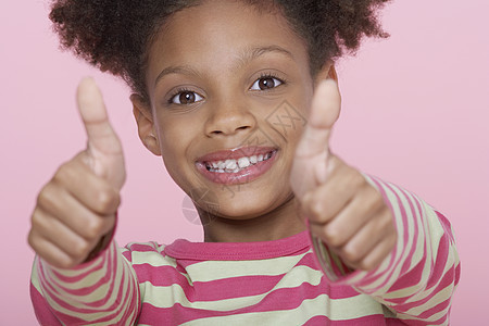 一个快乐女孩在粉红背景上 双拇指的特写肖像图片