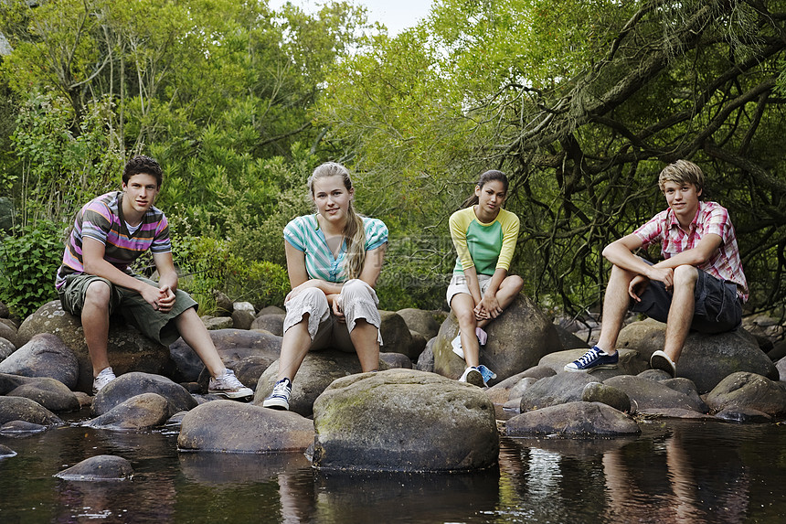 四位朋友坐在森林里河边的石块上图片