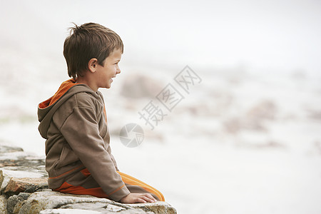 坐在沙滩墙上的小男孩的轮廓拍摄背景图片