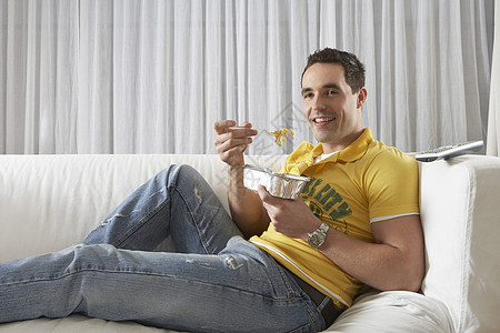 一位坐在沙发上吃着面条的年轻人的肖像图片