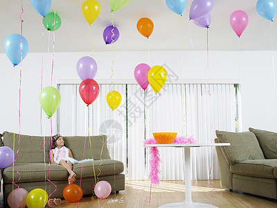一个女孩坐在客厅里坐满气球的全身年轻女孩孩子生日孩子们水平沉思童年庆典微笑闲暇派对图片