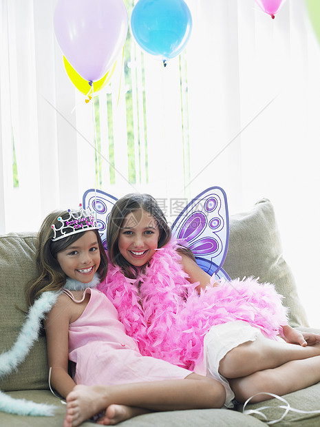 坐在沙发上穿着派对服装的 两个快乐少女的肖像长椅孩子生日戏服庆典闲暇蟒蛇团结微笑皇冠图片