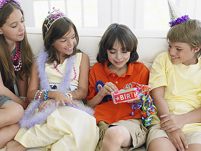 四个孩子在生日派对上坐在沙发上 一个打开礼物图片