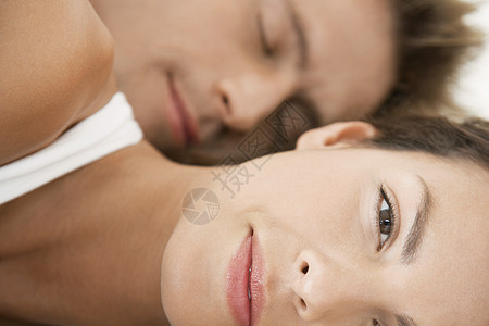 美丽的年轻女子与男人在背景中睡觉的近视肖像图片